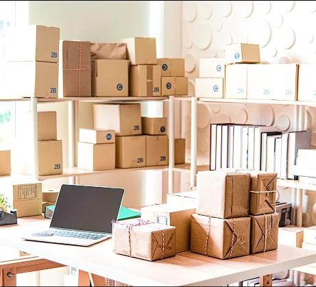 Packing station with stacked cardboard boxes, shelves and a laptop for order fulfillment.